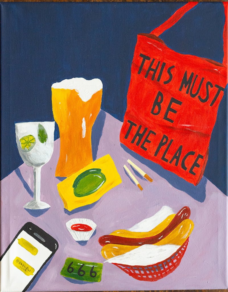 A painting of a table in The Hope & Ruin with a pint and a hot-dog